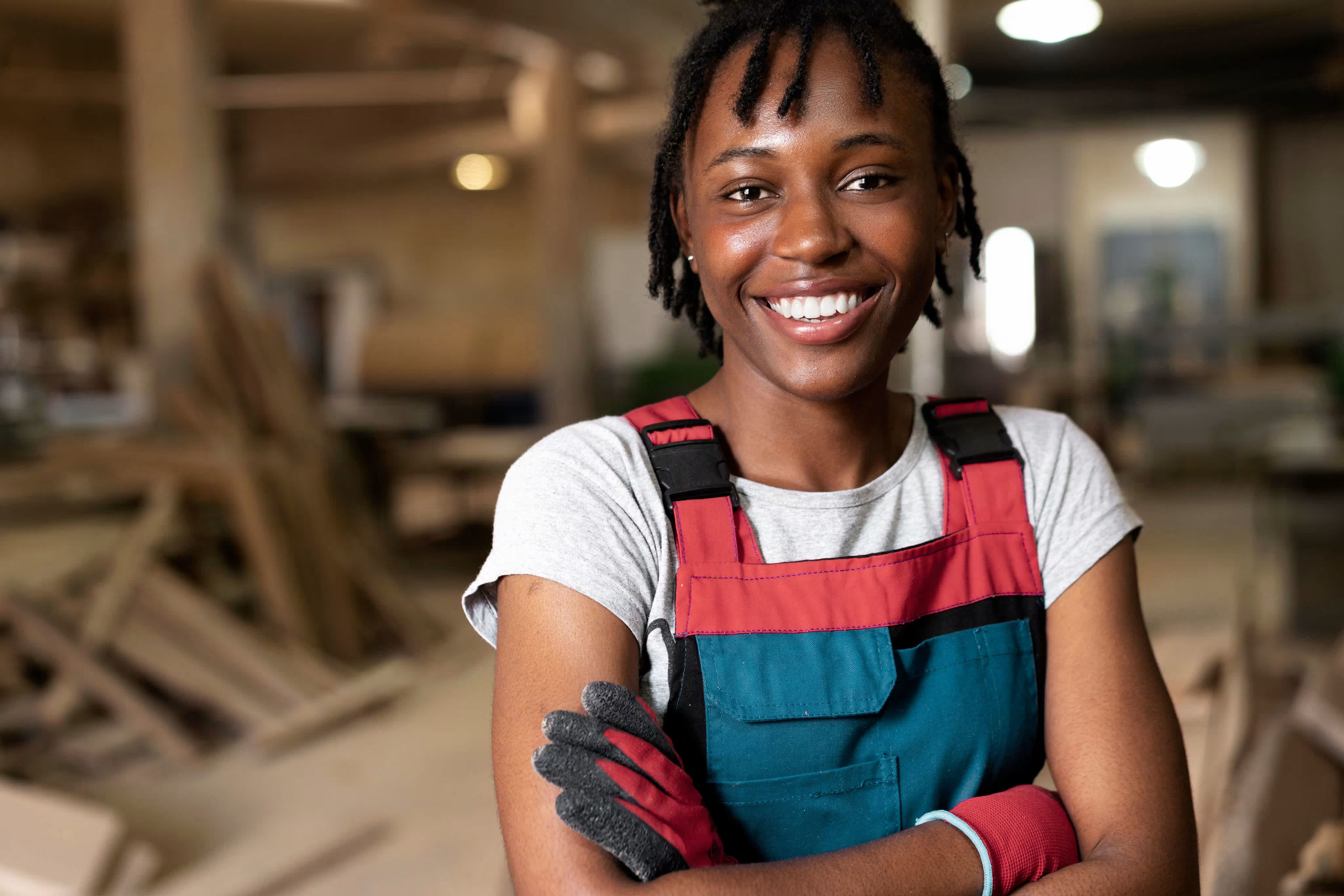 Smiling female carpenter with arms crossed in a woodworking shop surrounded by stacks of timber