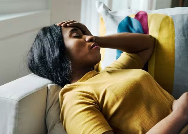 Woman lying on a couch with her hand on her forehead, looking stressed and fatigued