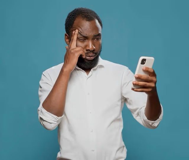 Frustrated man staring at his smartphone and rubbing his temple